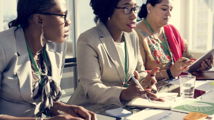 Three diverse women in suits sit at a table during a meeting.